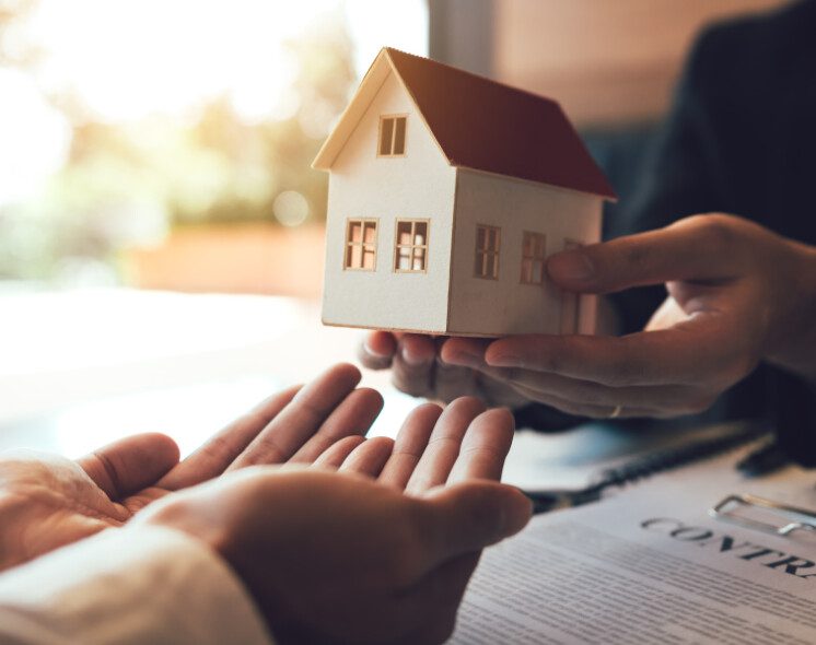 Duas pessoas de terno segurando um modelo de casa em miniatura, representando uma transação imobiliária ou a conclusão de um processo legal de adjudicação.